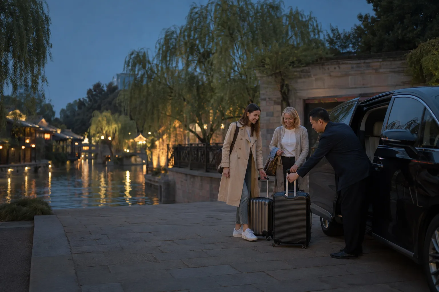 International travelers with suitcases meeting a local driver beside a canal-side water-town entrance at blue hour